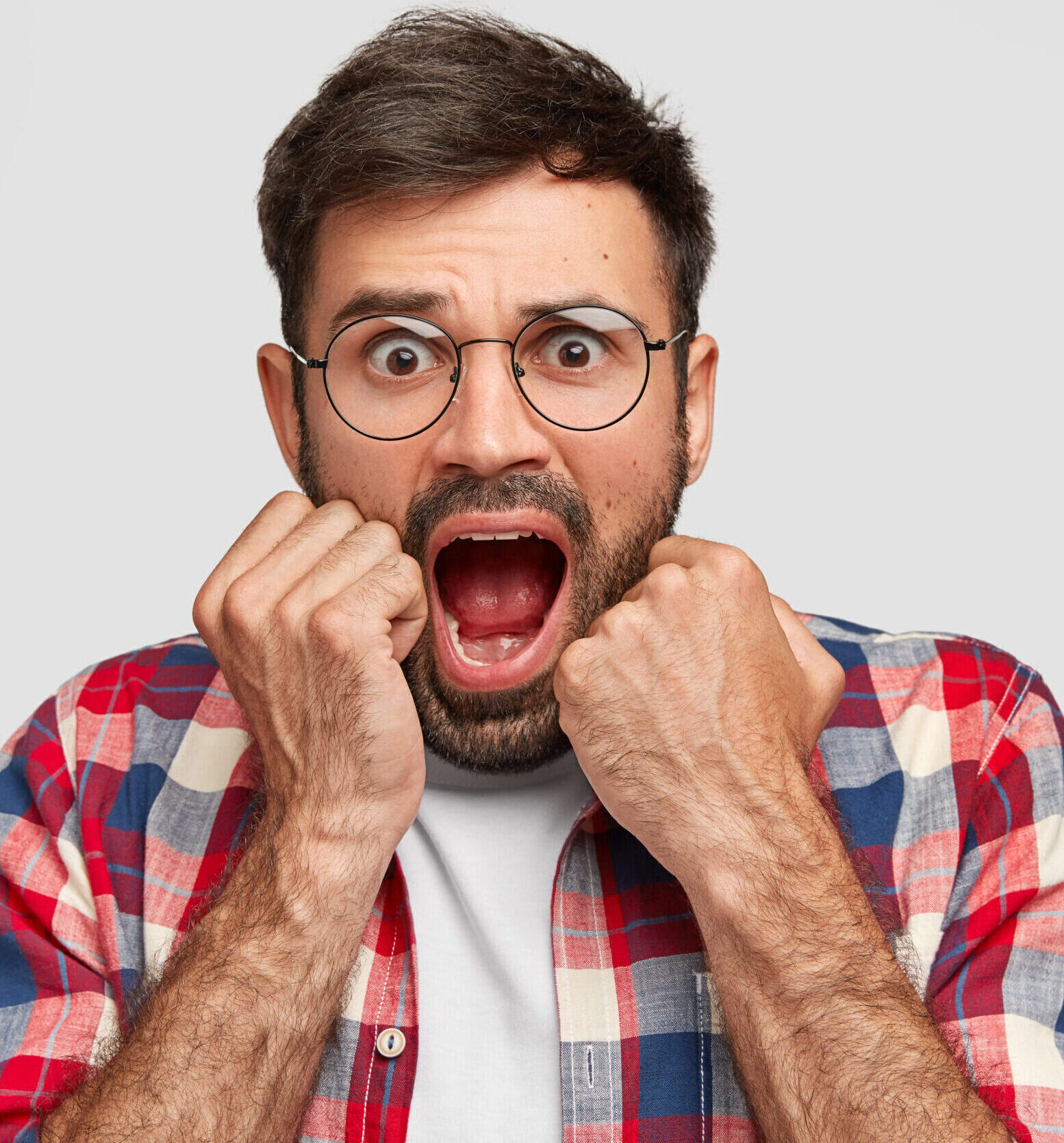 Stupefied handsome man looks with scared expression, keeps jaw dropped and hands near mouth, exclaims with fear, notices something terrific, isolated over white studio wall. Negative emotions