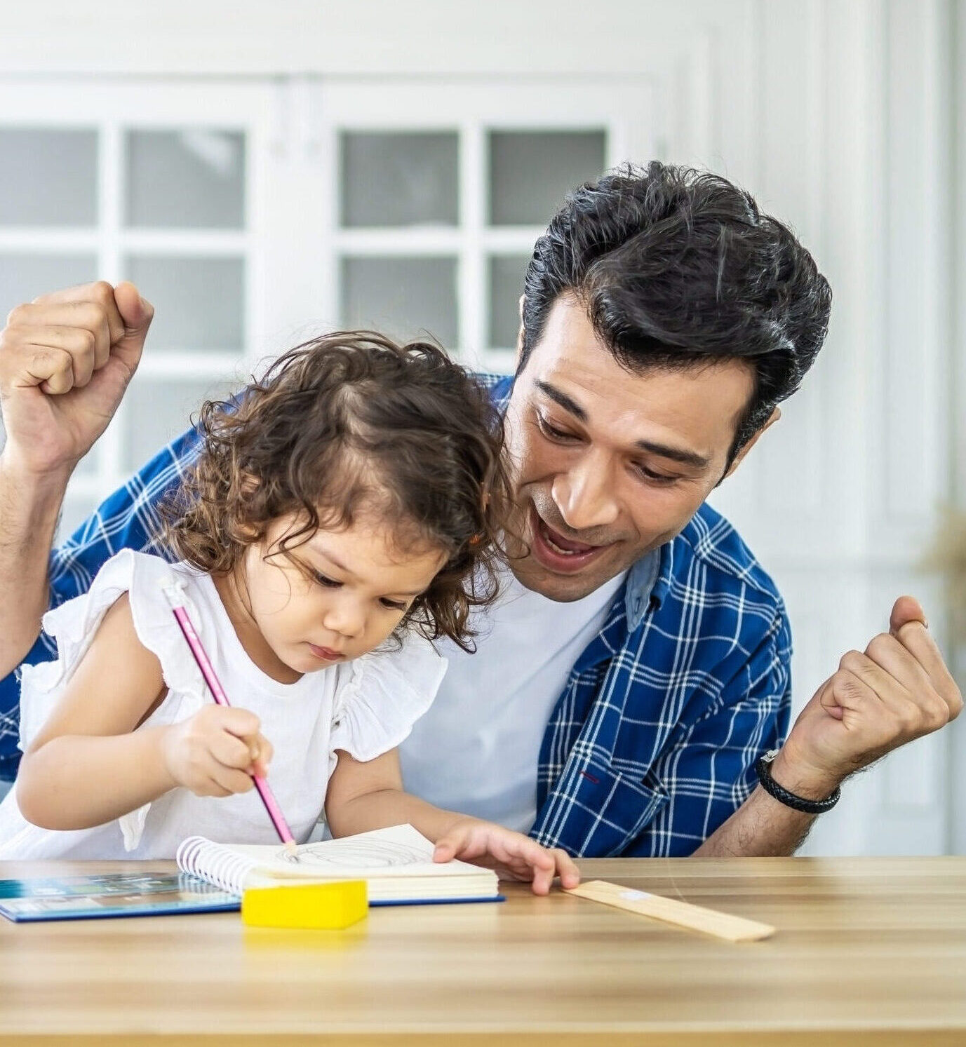 Portrait of young father teaching his cute little daughters' study. Excited smiling small child girl enjoying learning with pleasant dad at home. Children education, home schooling concept