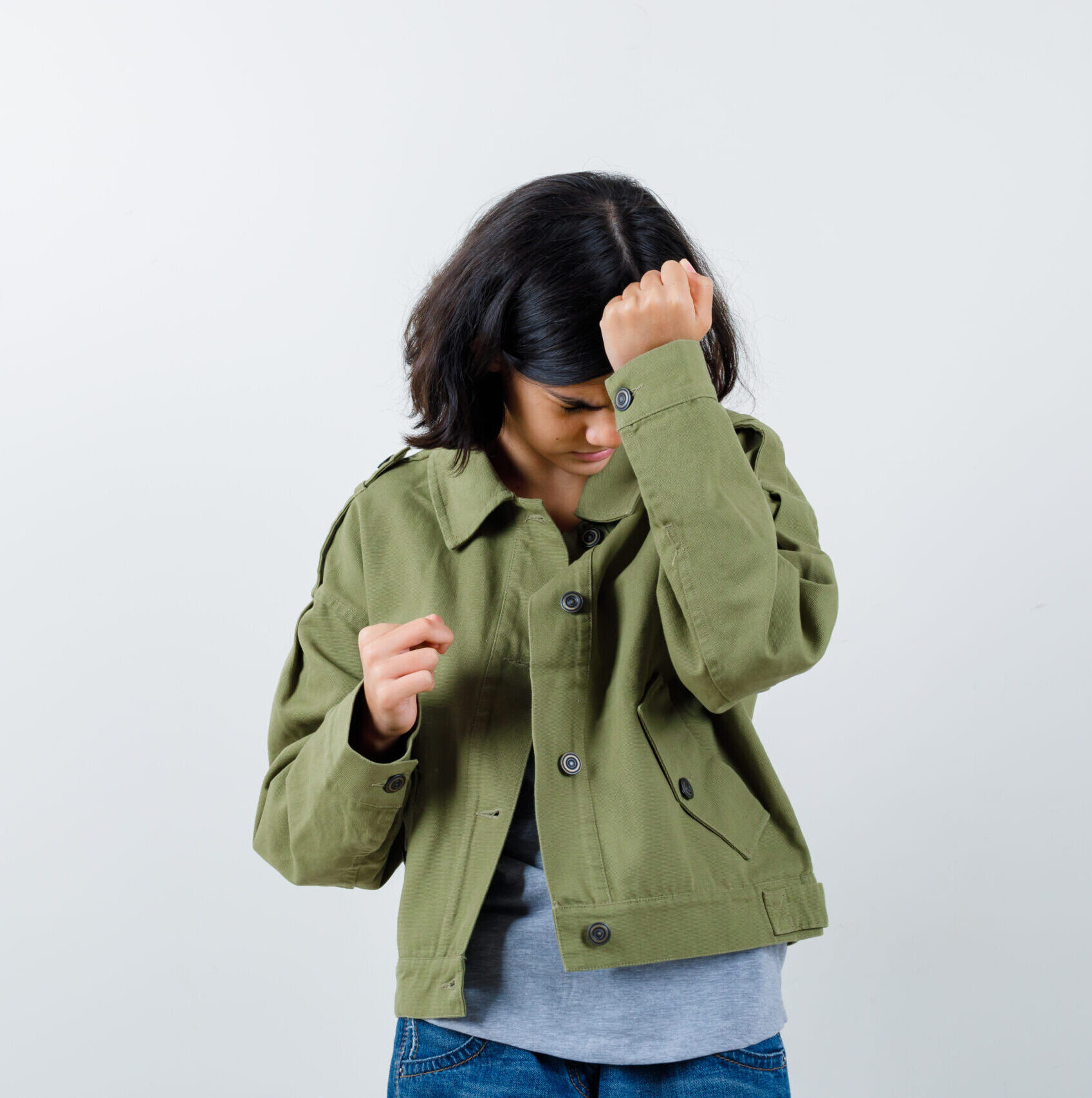 young girl clenching fist and putting hand on head in grey sweater, khaki jacket, jean pant and looking tired. front view.